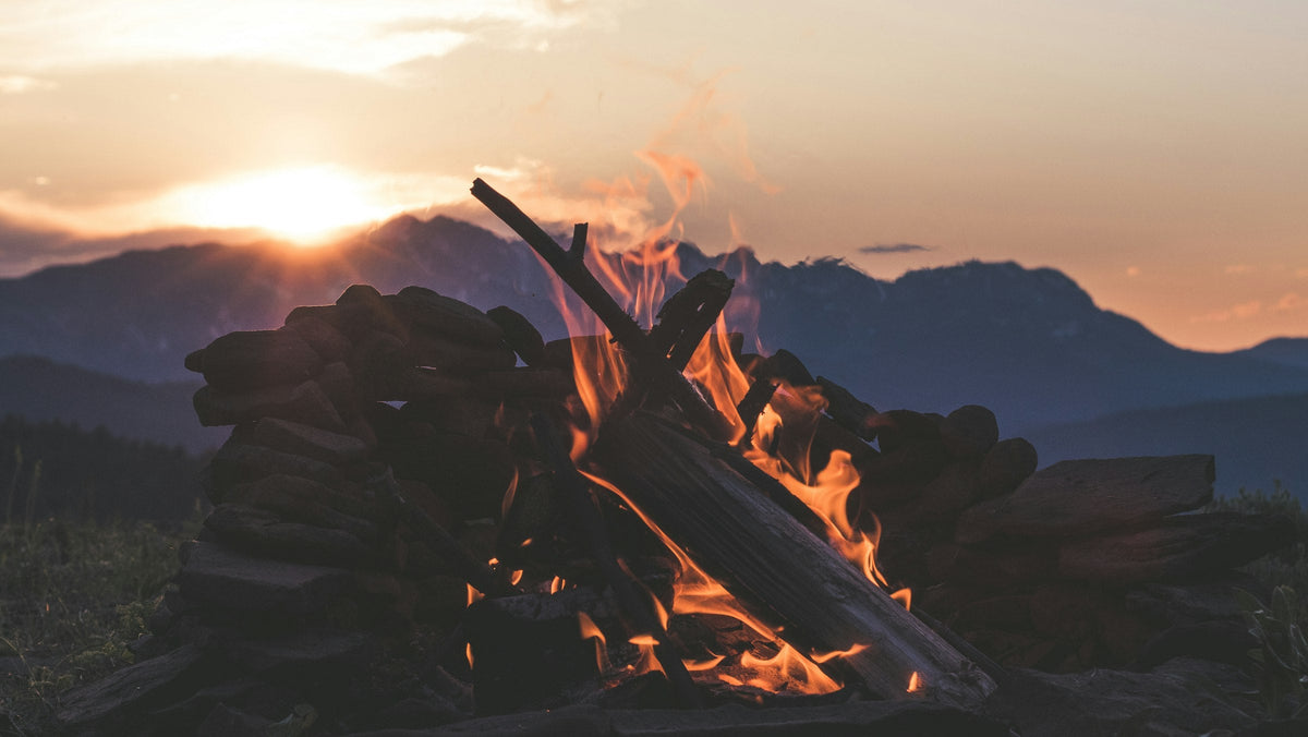 Brandend kampvuur met een rand van stenen bij zonsondergang in de bergen, het terrein waar een outdoor aansteker voor gemaakt is